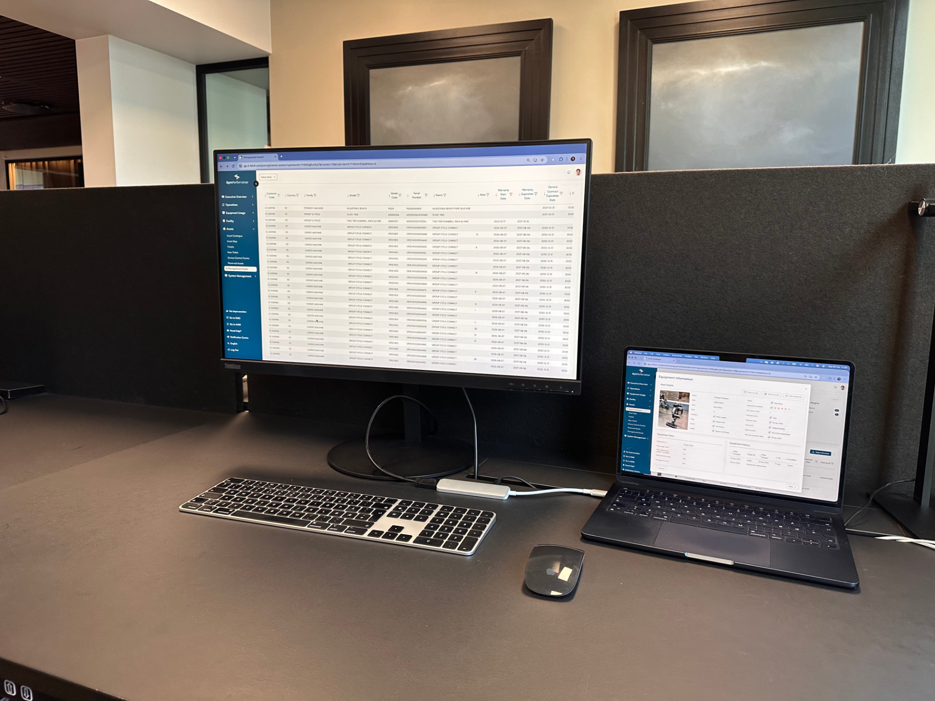 D-Fetch showing the equipment list on a desktop monitor and an asset's equipment information on a laptop, on a workplace desk